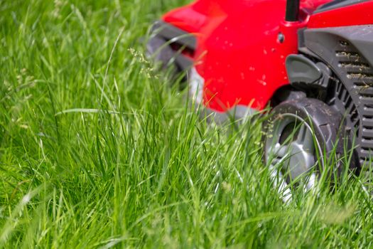 A close up image of a lawnmower on a lawn of long grass in need of cutting