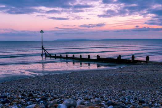 Sunset, groynes and silhouettes on the East Wittering shoreline, England, UK.