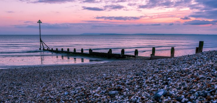 Sunset, groynes and silhouettes on the East Wittering shoreline, England, UK.