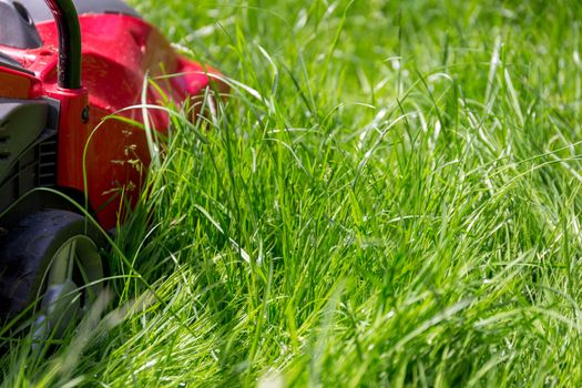 A close up image of a lawnmower on a lawn of long grass in need of cutting