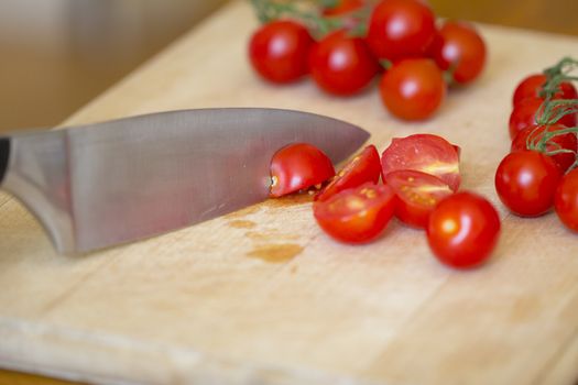 Cherry tomatoes (Solanum lycopersicum) and a knife on a wooden chopping board