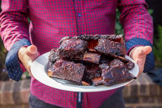 Man carrying a large plate of cooked beef short ribs from the barbecue