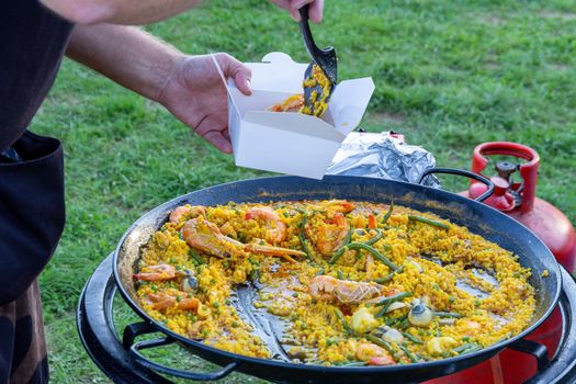 A large pan of seafood paella being served outdoors