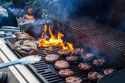 Marinated lamb joint and beef burgers cooking on a barbecue