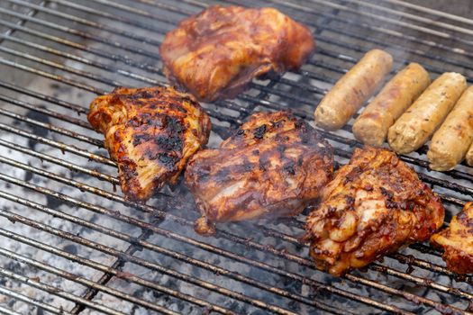 Marinated chicken pieces and vegetarian sausages being cooked on a barbecue