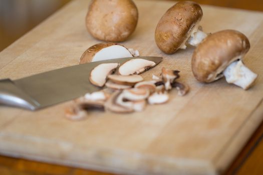Slicing Cremini mushrooms, agaricus risporus on a wooden chopping board