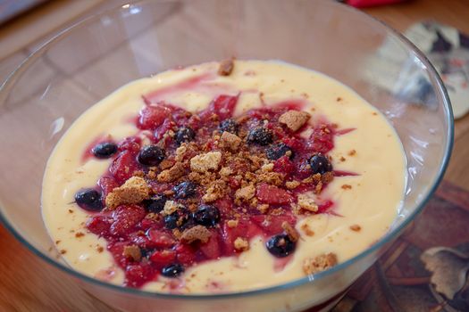 Homemade trifle with custard, strawberries, blueberries and crumbled biscuits