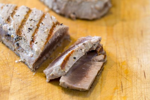 Chargrilled, seasoned tuna steaks cooked and sliced on a wooden chopping board