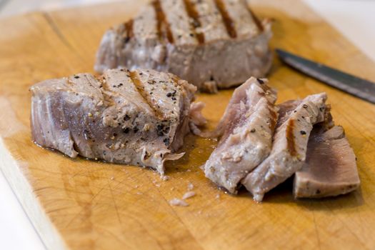 Chargrilled, seasoned tuna steaks cooked and sliced on a wooden chopping board