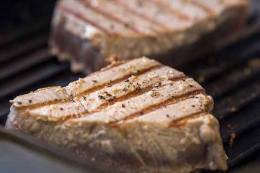 Close up of chargrilled tuna steaks cooking in a griddle pan with seasoning