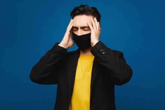 Young man in the black protective mask with headache. Handsome men holds hands on his head because of head pain. Portrait of sick man in medical mask touching painful head, medical concept. Healthcare.