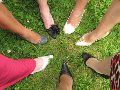 Shoes in a circle.  A group of formally dressed ladies in a circle with one shoed foot forward.