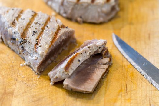 Chargrilled, seasoned tuna steaks cooked and sliced on a wooden chopping board