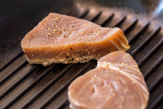 Close up of chargrilled tuna steaks cooking in a griddle pan with seasoning