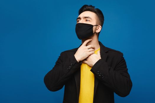 Young man in the black protective mask with throat sore. Handsome men holds hands on his neck because of throat pain. Inflamed throat. Portrait of sick man in medical mask touching painful neck, medical concept.