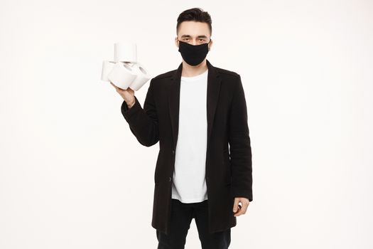 Handsome young man in black protective mask holding four rolls of toilet paper, isolated on the white background. Young men in protective face mask keeps rolls of toilet paper.