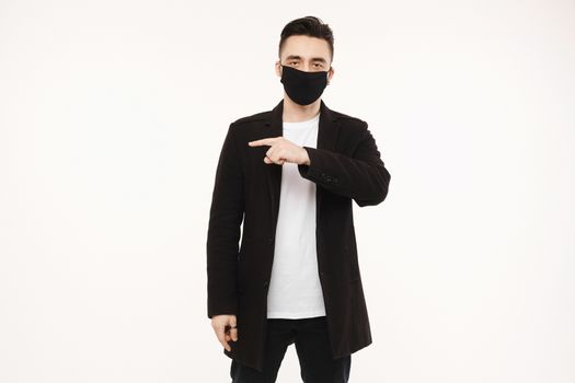 Handsome men in black protective mask pointing finger to the left side of the shot, isolated on the white background with copy space. Lifestyle protective against viruses, seasonal illness and air pollution. Healthcare concept.