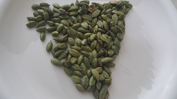 Closeup top view of dried green Elettaria cardamomum fruits with seeds, cardamom spice arranged in triangle on a white background