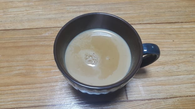 Top view of hot milk tea or black tea in a dark brown ceramic cup placed over a wooden floor.