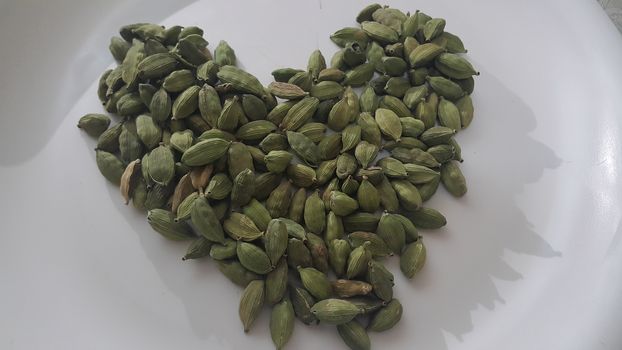 Closeup top view of dried green Elettaria cardamomum fruits with seeds, cardamom spice arranged in heart shape on a white background