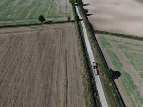 drone view of a tractor and trailer on a long rural road between flat ploughed fields