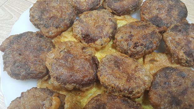 Delicious spicy fried round kebab served in a white ceramic plate on wooden floor, Asian recipe