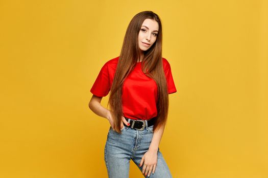 Young woman with slim body in a red blank t-shirt and jeans isolated at the yellow background.