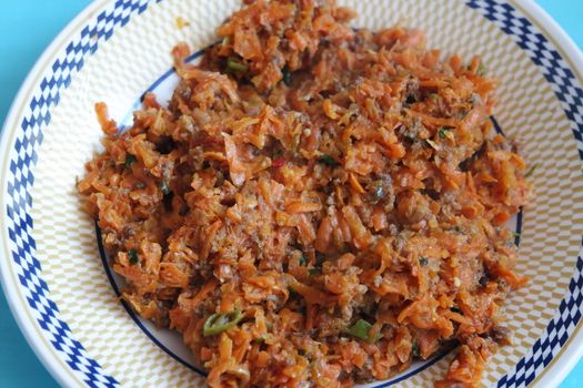 Top closeup view of a homemade dish made from carrot and vegetables served in a ceramic plate.