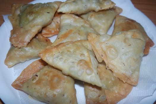 Closeup of delicious home made spicy and crunchy samosa pastries placed in a white ceramic plate on wooden floor