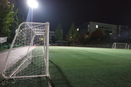 Night view of a soccer goal net under flood lights. Closeup view of goal net in a soccer playground