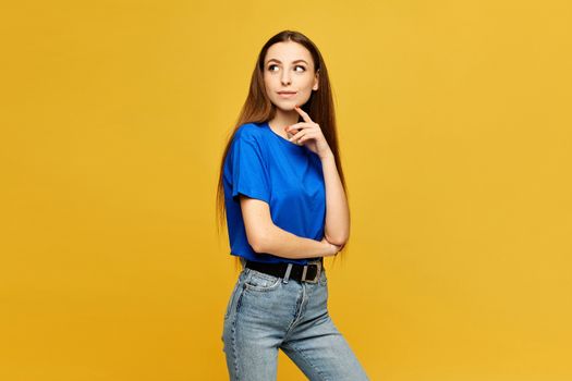 Young model with slim body in a blue oversized t-shirt and jeans looking aside and posing at the yellow background, isolated.