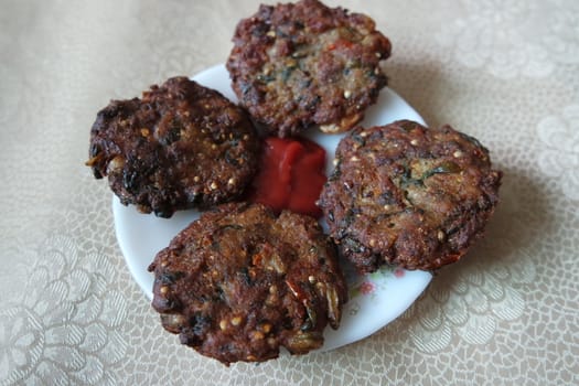 Delicious spicy fried round kebab served in white ceramic plate on a wooden floor with red sauce.