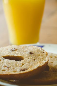 A glass of orange juice and a sliced toasted raisin and cinnamon bagel