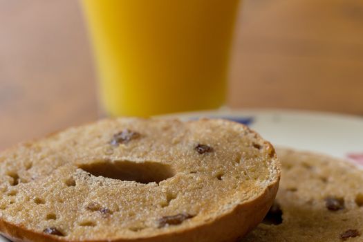 A glass of orange juice and a sliced toasted raisin and cinnamon bagel