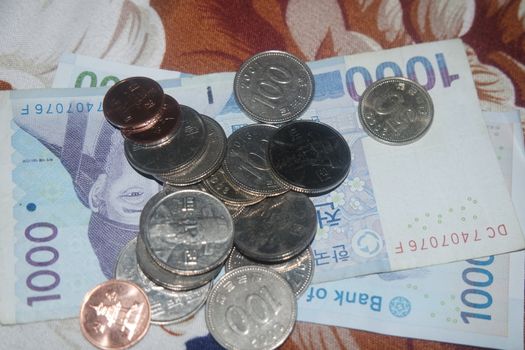 Silver shining Korean won coin scattered over Korean notes on a wooden floor.