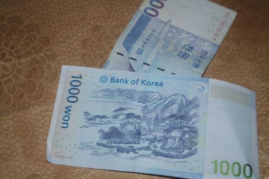 Silver shining Korean won notes scattered over a wooden floor.