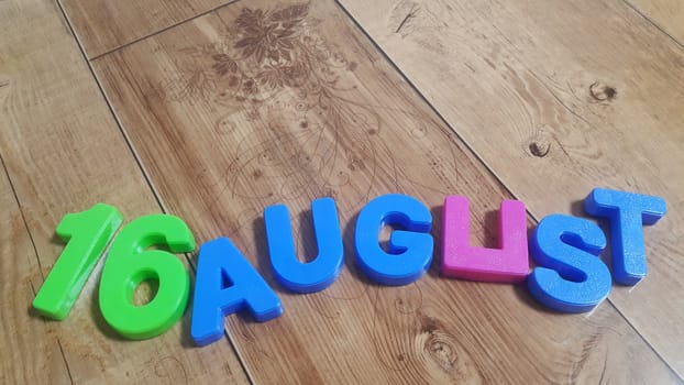 Plastic colored alphabets making words 16 August are placed on a wooden floor. These plastic letters can be used for teaching kids.