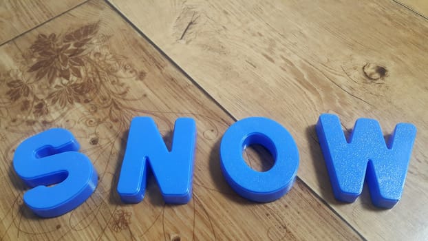 Plastic colored alphabets making words are placed on a wooden floor. These plastic letters can be used for teaching kids.