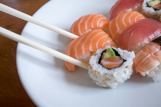 Fresh salmon nigiri sushi between chopsticks along with uramaki, prawn nigiri and tuna nigiri