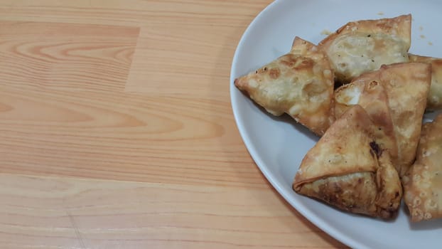 Closeup of delicious home made spicy and crunchy samosa pastries placed in a white ceramic plate on wooden floor