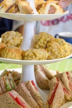English afternoon tea consisting of sandwiches, cheese scones and sausage rolls on a tiered cake stand