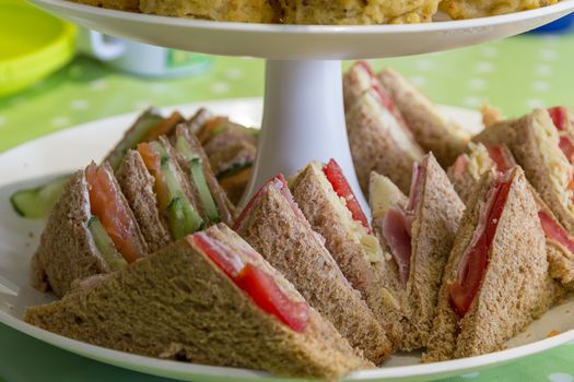 English afternoon tea consisting of sandwiches, cheese scones and sausage rolls on a tiered cake stand