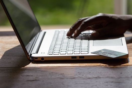A black man conducting an online transaction with laptop and credit card