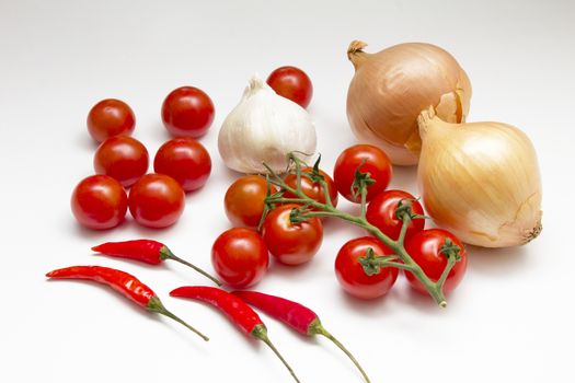 An arrangement of onons, tomatoes, chillies and garlic on a white background