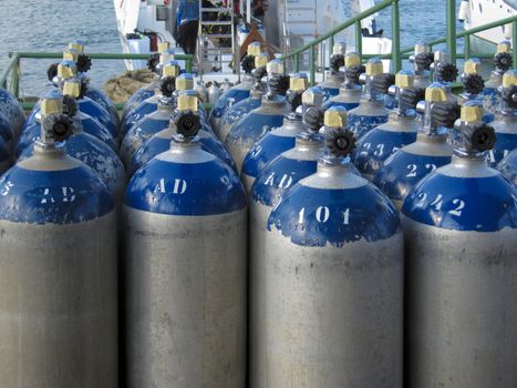 Rows of oxygen storage tanks used for scuba diving, with dive boats in the background.