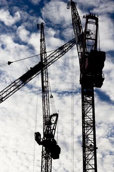 Three tower cranes silhouetted against a cloud filled sky