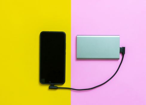 Smartphone mobile phones charging batteries by power bank pink and yellow background