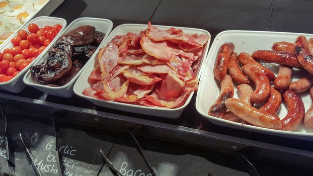 English breakfast buffet with bacon, sausages, eggs and tomatoes