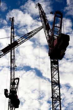 Three tower cranes silhouetted against a cloud filled sky