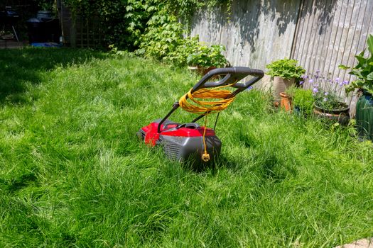 A lawnmower on a lawn of long grass in need of cutting